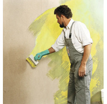 Handwerker streicht eine Wand mit einem Fassadenpinsel und Wandfarbe in Innenbereich.