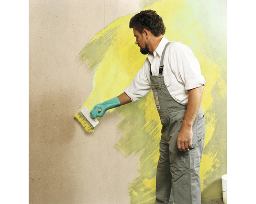 Handwerker streicht eine Wand mit einem Fassadenpinsel und Wandfarbe in Innenbereich.