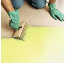Person mit Handschuhen streicht eine Fläche mit einem großen Flächenstreicher aus Holz.