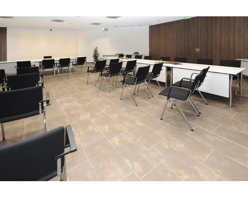 Konferenzraum mit rechteckigen Tischen, Stühlen und Fliesenboden in einer geschäftlichen Umgebung.