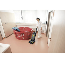Reinigungskraft bedient eine Kärcher Scheuersaugmaschine in einem hellen Badezimmer mit einer medizinischen Wanne.