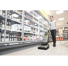 Eine Frau bedient eine Kärcher Bodenreinigungsmaschine in einem Supermarkt vor einem Getränkekühlregal.