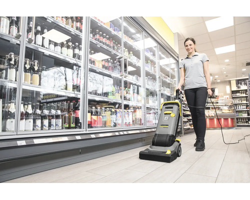 Eine Frau bedient eine Kärcher Bodenreinigungsmaschine in einem Supermarkt vor einem Getränkekühlregal.