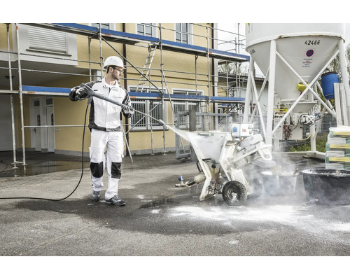 Handwerker reinigt professionelle Mörtelmaschine auf einer Baustelle mit einem Hochdruckreiniger.