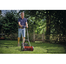 Ein Mann schiebt einen manuellen Handrasenmäher mit Grasfangkorb über eine Rasenfläche in einem Garten.