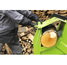 Eine Person benutzt eine Wippsäge zum Sägen eines Baumstammes vor einem Holzstapel.