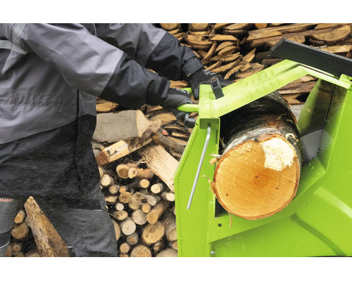 Eine Person benutzt eine Wippsäge zum Sägen eines Baumstammes vor einem Holzstapel.