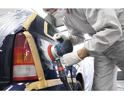 Ein Arbeiter schleift mit einem Schleifer ein Auto in einer Werkstatt.