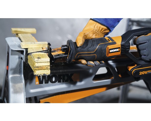 Akkubetriebene Säbelsäge beim Sägen von Holz auf einem Arbeitstisch, von einer Person mit Handschuhen bedient, Worx Logo sichtbar.