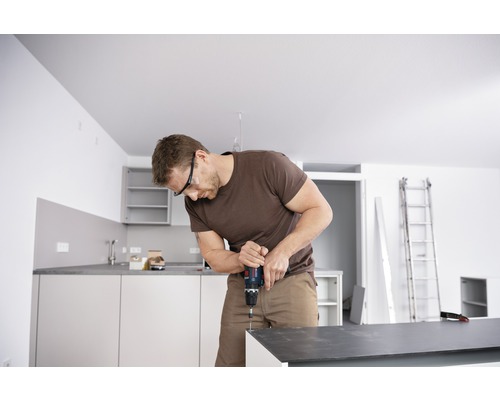 Mann montiert Küche mit Akkubohrer und Schutzbrille