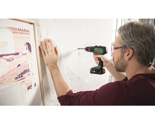 Ein Mann bohrt mit einem Akku-Bohrschrauber ein Loch in eine Wand.