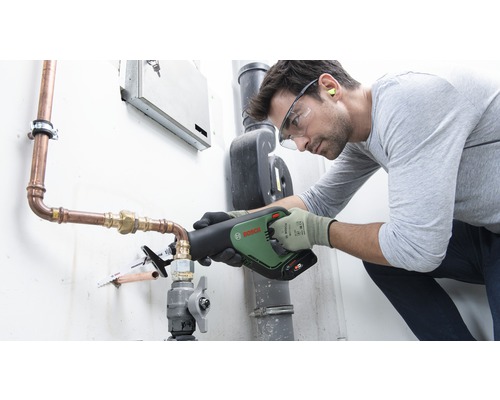 Ein Handwerker verwendet eine Säbelsäge von Bosch, um ein Kupferrohr zu schneiden. Er trägt Schutzkleidung wie Schutzbrille und Handschuhe.