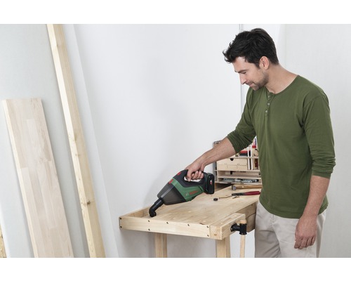 Ein Mann saugt mit einem Akku-Handsauger eine Holzwerkbank ab.