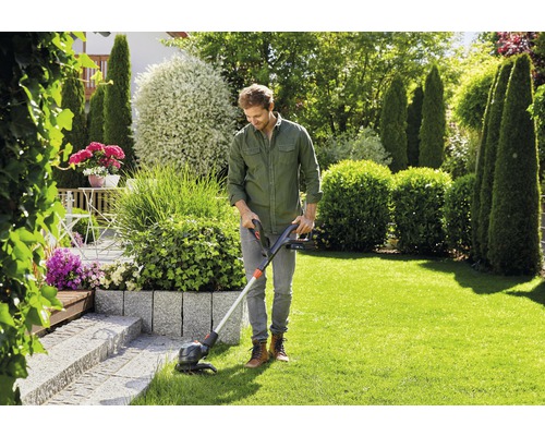 Mann trimmt Rasen mit Rasentrimmer im Garten