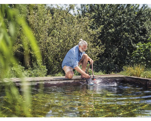 Ein Mann reinigt einen Teich mit einer Teichbürste von Algen und Schmutz.