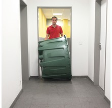 Eine Person transportiert einen grünen Kompostbehälter in einem Flur.