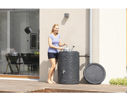 Frau befüllt Gießkanne an Regentonne im Garten