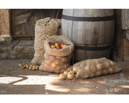 Verschiedene Säcke mit Äpfeln, Kartoffeln und Zwiebeln neben einem Holzfass