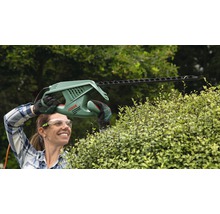Frau schneidet Hecke mit einer elektrischen Heckenschere der Marke Bosch.