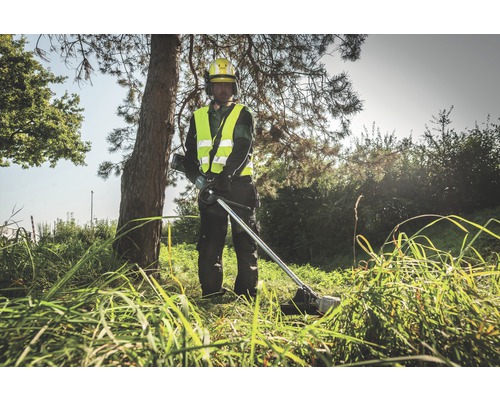 Mann mit gelbem Schutzhelm und Warnweste bedient einen Rasentrimmer im Gras.