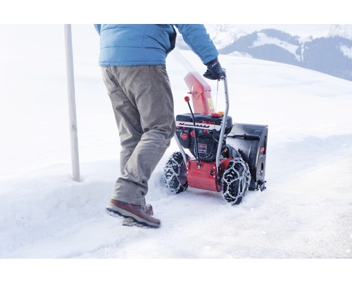 Eine Person schiebt eine Schneefräse auf einer verschneiten Fläche.