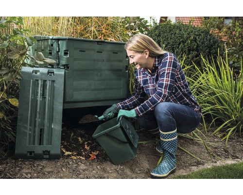Eine Frau befüllt einen Thermokomposter im Garten mit Gartenabfällen.
