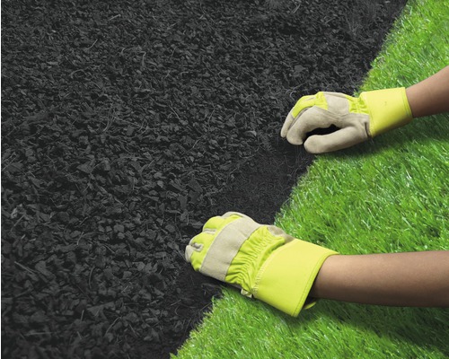 Zwei Hände mit Arbeitshandschuhen verlegen Mulch neben Kunstrasen.