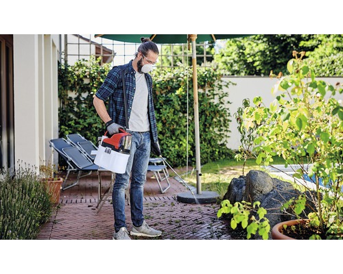 Mann mit Schutzmaske und Gartenspritze zur Unkrautbekämpfung auf einer Terrasse
