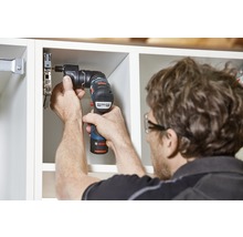 Eine Person befestigt mit einem Akku-Bohrschrauber eine Möbeltür an einem Schrank.