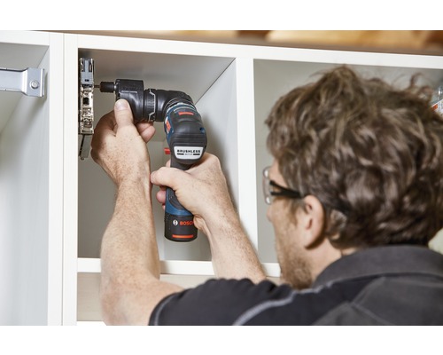Eine Person befestigt mit einem Akku-Bohrschrauber eine Möbeltür an einem Schrank.