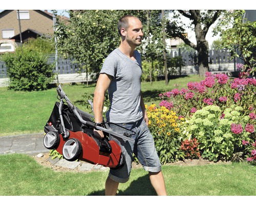 Mann trägt einen Vertikutierer durch den Garten