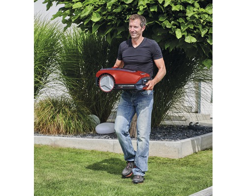 Mann trägt einen roten Rasenmähroboter im Garten.