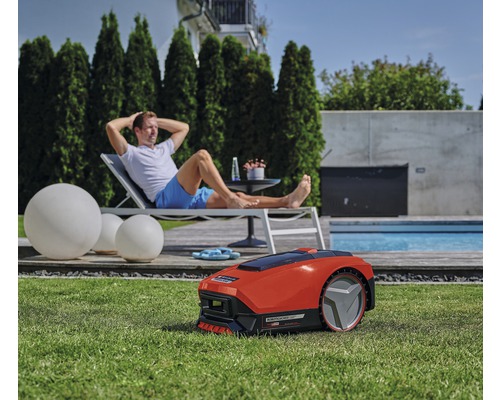 Rasenzene mit einem Mann, der auf einer Liege entspannt, während ein Rasenmähroboter das Gras mäht