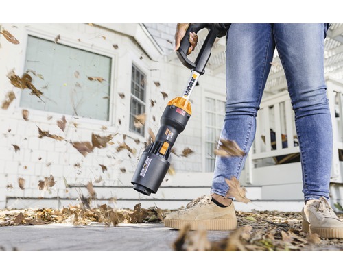 Eine Person benutzt einen Akku-Laubsauger zum Entfernen von Laub auf einem Gehweg.
