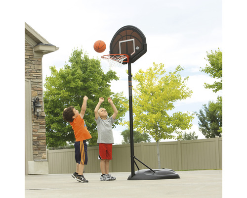 Zwei Kinder spielen mit einem Basketballkorb im Garten.