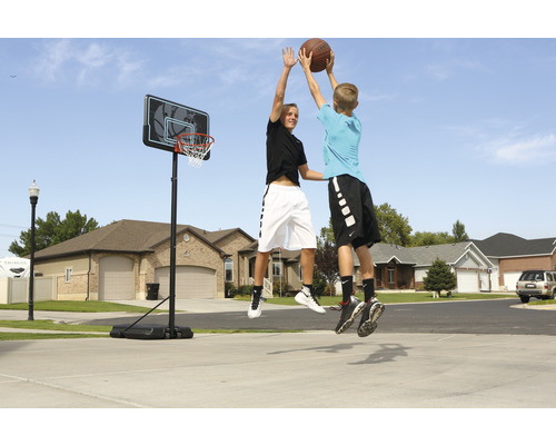 Zwei Jugendliche springen, um einen Basketball in einen Basketballkorb im Freien zu werfen.