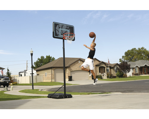 Ein Junge springt, um einen Basketball in einen mobilen Basketballkorb im Freien zu werfen.
