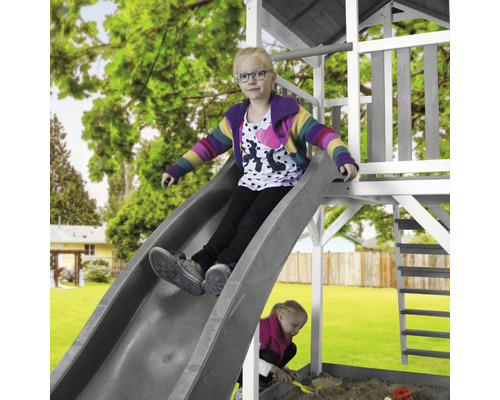 Kind auf einer Rutsche eines Spielgerüsts im Garten.