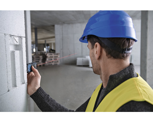 Ein Mann mit Schutzhelm verwendet einen Laser-Entfernungsmesser auf einer Baustelle zur Messung.