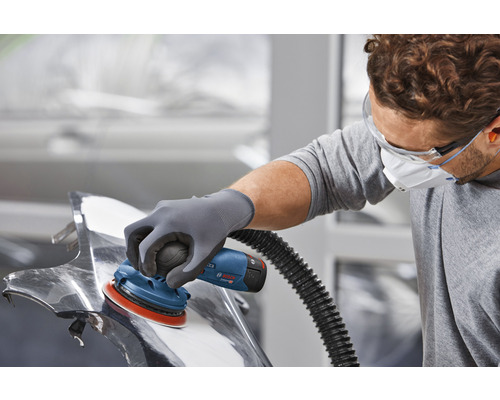 Ein Mann schleift mit einem Exzenterschleifer ein Werkstück aus Metall.