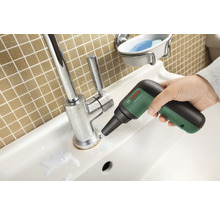 Ein Waschbecken wird mit einer elektrischen Reinigungsbürste gesäubert. Im Hintergrund befindet sich eine Wand mit quadratischen Fliesen.