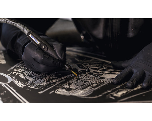 Detailaufnahme einer Person, die mit einem Dremel Gravuren in eine dunkle Oberfläche einritzt