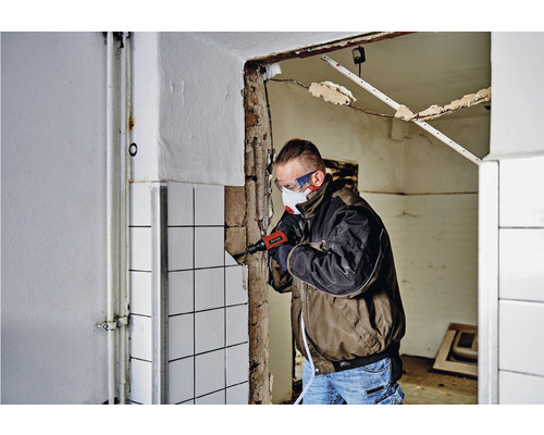 Mann entfernt Fliesen mit einem elektrischen Fliesenschneider, persönliche Schutzausrüstung wird getragen