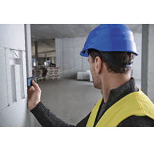 Ein Mann mit Schutzhelm und Warnweste verwendet einen Laser-Entfernungsmesser auf einer Baustelle.