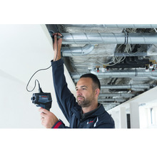 Ein Mann inspiziert mit einer Inspektionskamera Rohrleitungen unter einer Decke.