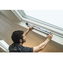 Ein Mann benutzt eine digitale Wasserwaage an einem Dachfenster.