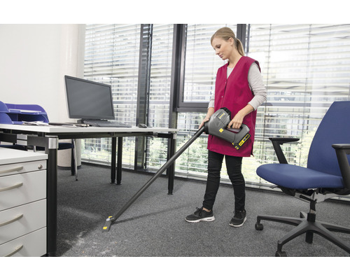 Eine Frau saugt mit einem Akkusauger einen Teppich in einem Büro.