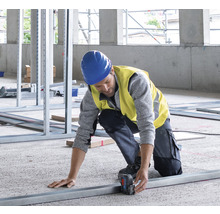 Ein Bauarbeiter misst ein Metallprofil mit einem Laser-Entfernungsmesser auf einer Baustelle
