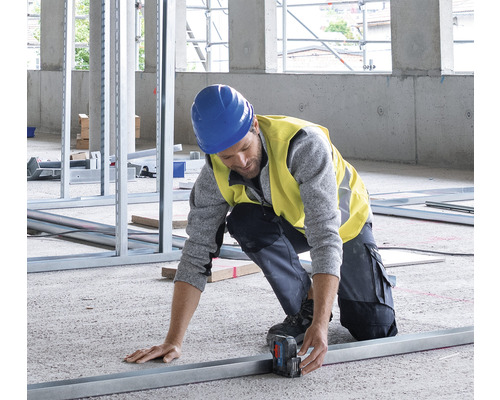 Ein Bauarbeiter misst ein Metallprofil mit einem Laser-Entfernungsmesser auf einer Baustelle