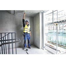 Ein Mann mit Schutzhelm und Warnweste verwendet einen Punktlaser zur Ausrichtung in einem Rohbau.